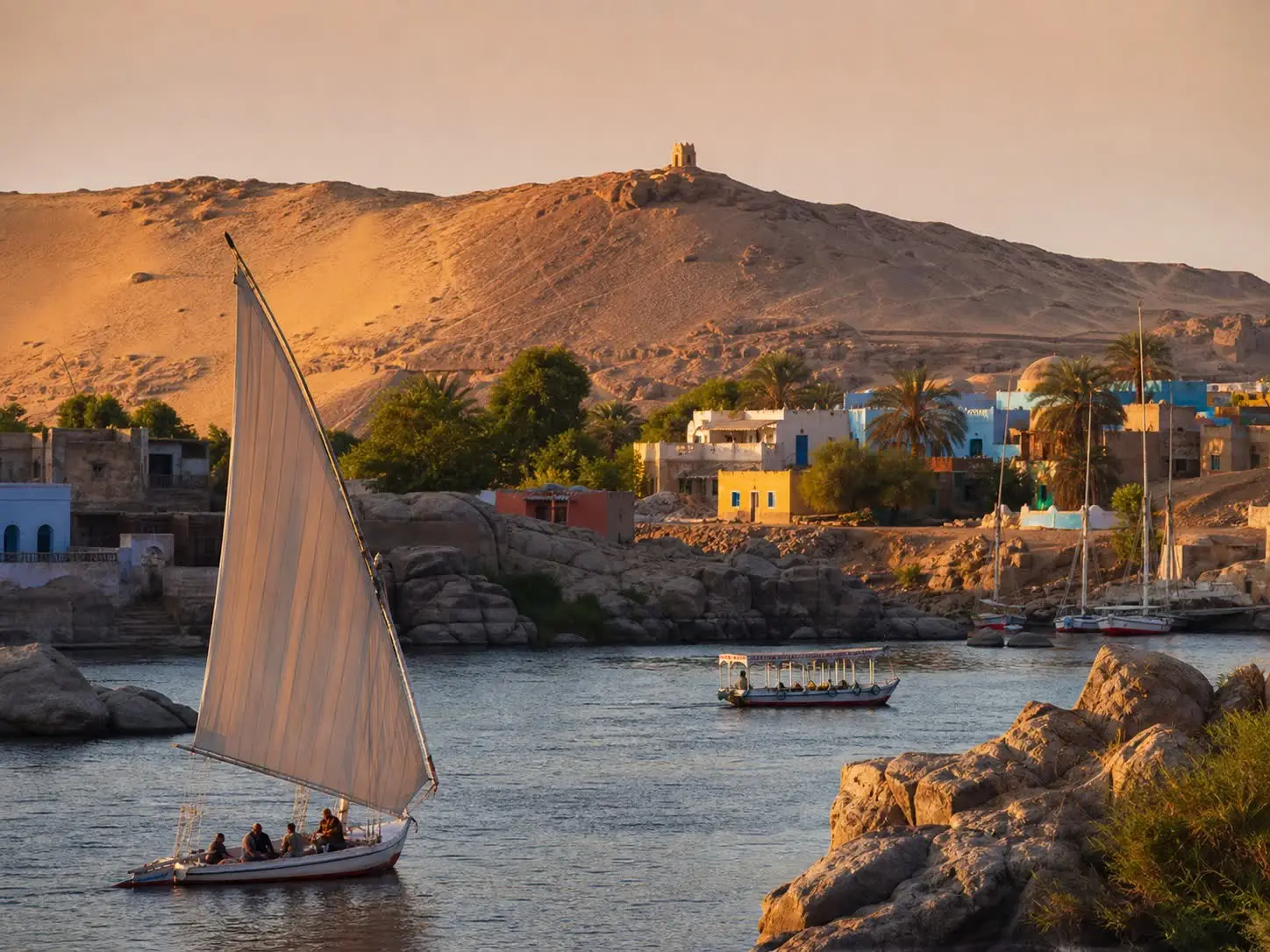 Een felucca zeilt in avondlicht langs het Nubische dorp op Elephantine bij Aswan